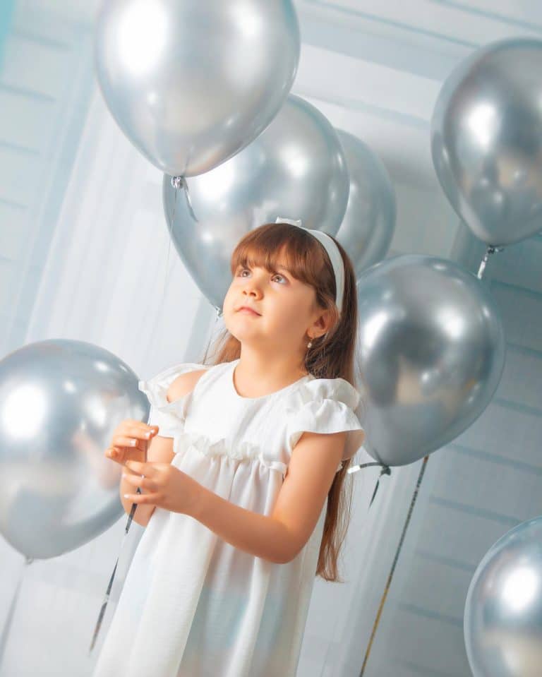 کودکی در میان بادکنک های نقره ای رنگ برای عکاسی در روز تولدش در استودیو