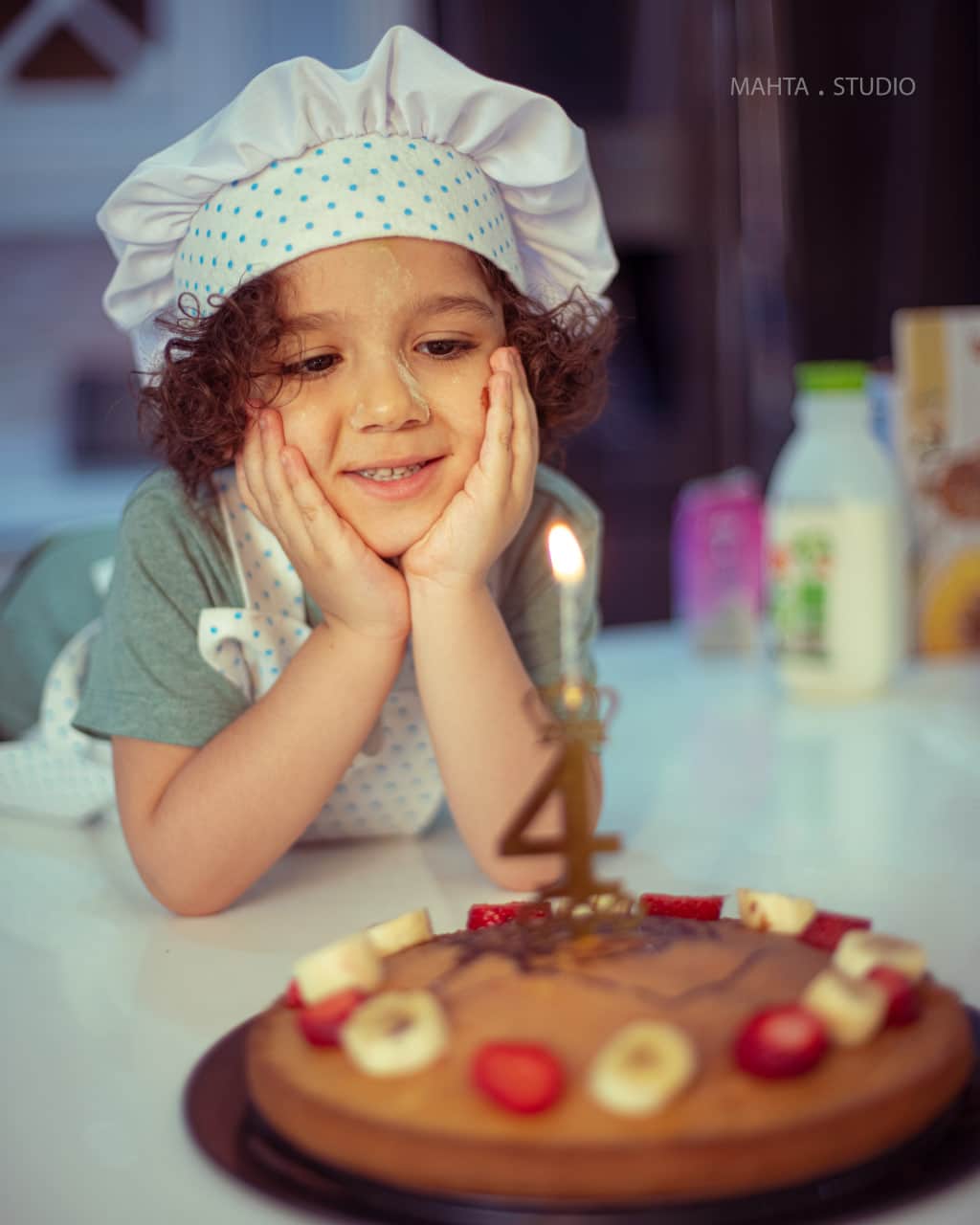 یک عکس آتلیه از کودک در حال خیره شدن به کیک تولد