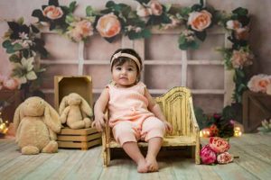 دختر بچه ای در پس زمینه گل های بهاری و پنجره نشسته