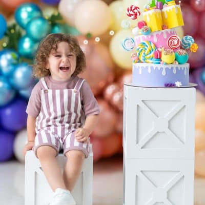 کودکی در حال خندیدن در فضای شاد بادکنکی در کنار یک کیک تولد طرح آبنباتی