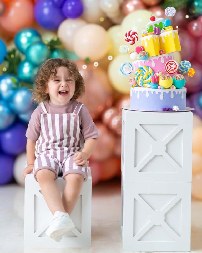 کودکی در حال خندیدن در فضای شاد بادکنکی در کنار یک کیک تولد طرح آبنباتی