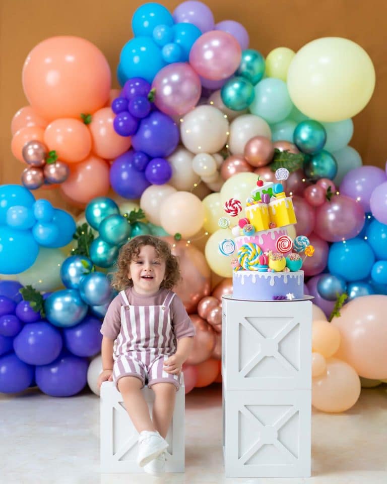 کودکی در حال خندیدن در فضای شاد بادکنکی در کنار یک کیک تولد طرح آبنباتی