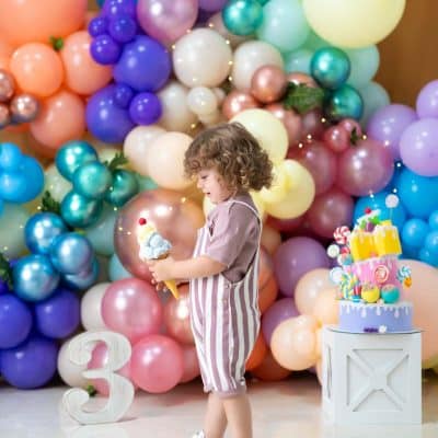 کودکی در حال خندیدن در فضای شاد بادکنکی در کنار یک کیک تولد طرح آبنباتی